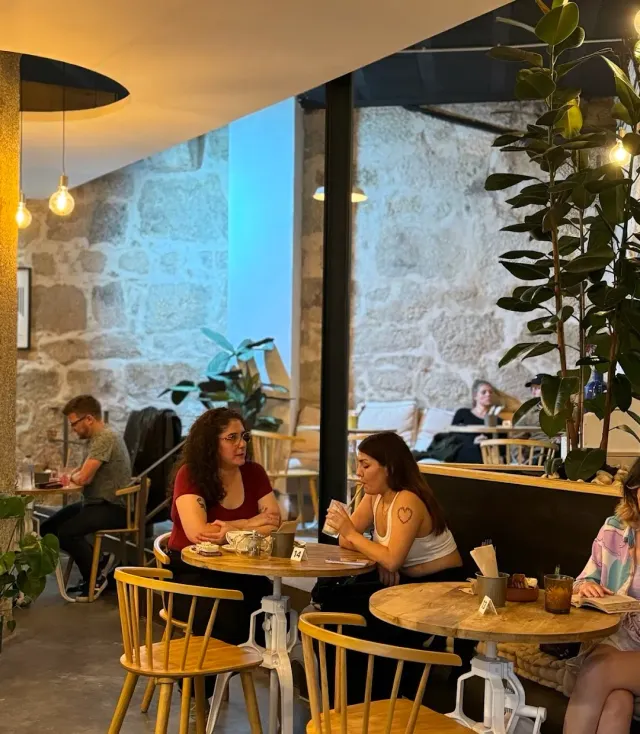 חלל עם קירות אבן, שולחנות עגולים, כיסאות עץ צהובים ויושבים משוחחים