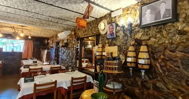 אולם עם קירות אבן גסה, תמונות ממוסגרות, חביות קטנות ושולחנות במפות לבנות