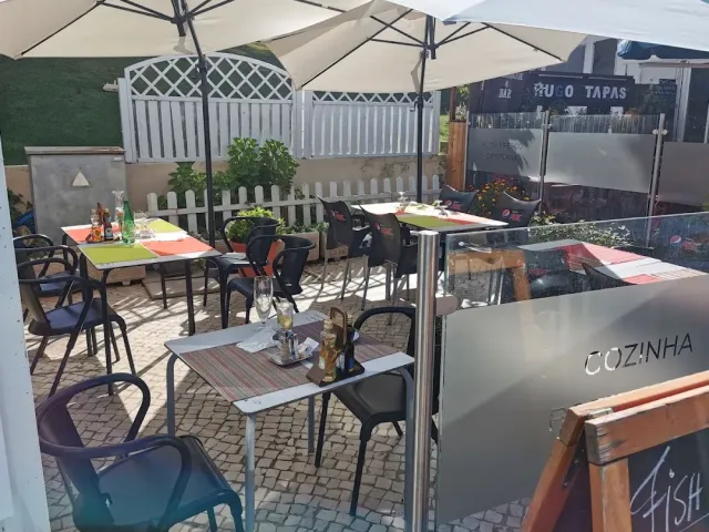 חצר מרוצפת עם שמשיות לבנות, שולחנות בצבעים וגדר עץ לבנה סביב