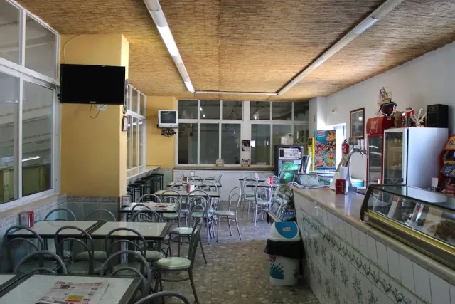 חלל פשוט עם שולחנות פורמייקה, כיסאות מתכת, דלפק מקורר ומסך על הקיר