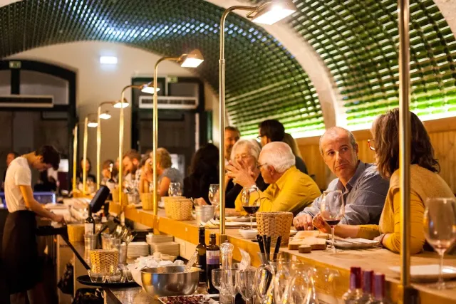 תקרה מקומרת מרופדת בקבוקים ירוקים מעל דלפק ארוך עם סועדים