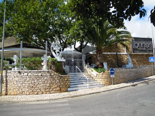 מבנה לבן מאחורי קיר אבן, מדרגות, פסלים לבנים ועצי דקל