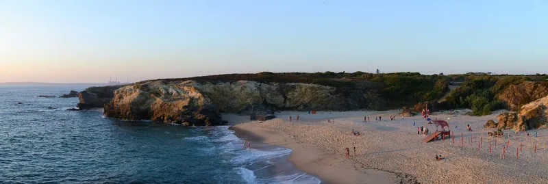 מפרץ חול מוקף צוקים נמוכים עם גלים לבנים באור שקיעה רך