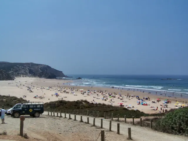 חוף גלים רחב עם מתרחצים ושביל דיונות בחזית