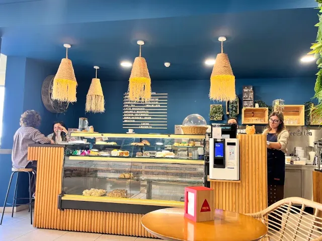 חלל עם קיר כחול עמוק, מנורות גדילים צהובות וויטרינת עוגות מול הדלפק