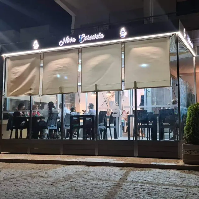 חזית מוארת בלילה עם קיר זכוכית, סועדים בפנים ושלט אותיות מוארות
