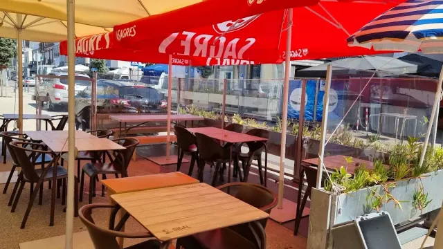 שולחנות חוץ תחת שמשיות אדומות מול כביש ומחיצת זכוכית
