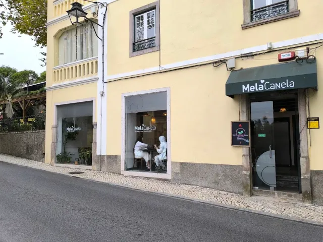 מבנה צהוב ברחוב משופע עם סוכך ירוק כהה ושני יושבים ליד החלון