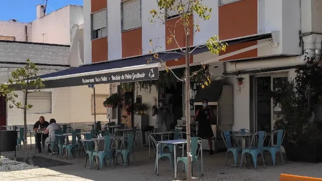 כיסאות מתכת בטורקיז סביב שולחנות על מרצפת רחוב, מתחת לסוכך כחול
