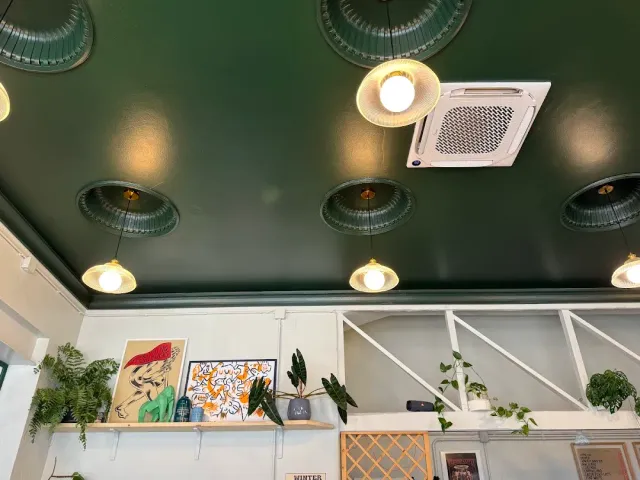 מבט אל תקרה ירוקה כהה עם מנורות מתכת ירוקות, ומדף כרזות וצמחים