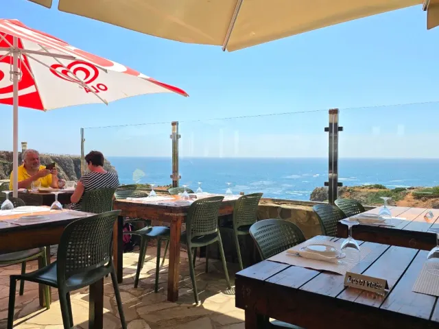 מרפסת עם שמשיות וכיסאות ירוקים מעל האוקיינוס, סועדים יושבים ליד המעקה