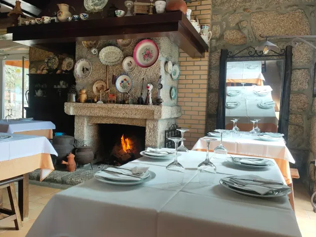 אח אבן גדולה עם אש בוערת וצלחות נוי, מול שולחנות במפות לבנות
