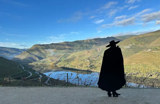 צללית דמות בגלימה וכובע רחב מול עיקול נהר בין מדרונות כרמים