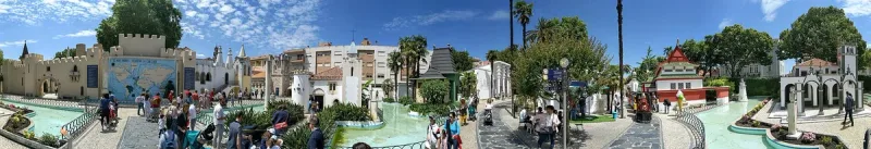 בריכת מים ומבנים מוקטנים בין דקלים בפארק שטוף שמש