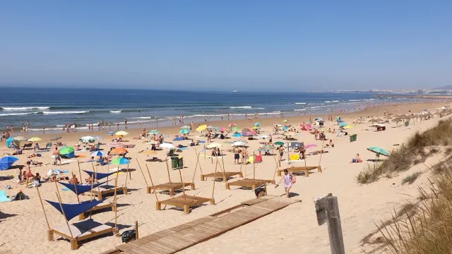 חוף חול רחב עם שמשיות, מיטות שיזוף ושביל עץ אל הגלים