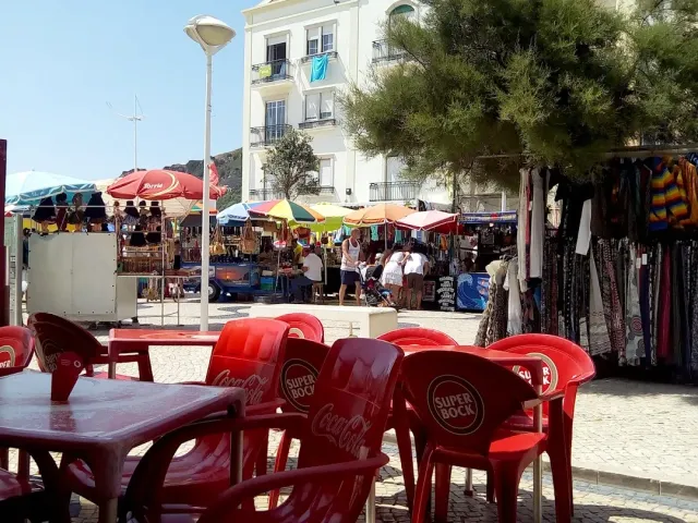 כיסאות פלסטיק אדומים בכיכר מרוצפת מול דוכנים עם שמשיות צבעוניות