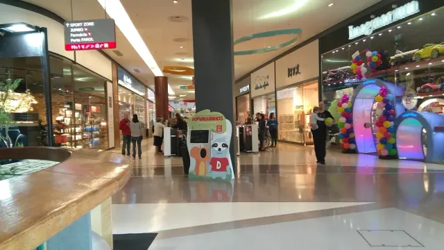 מסדרון קניון מרוצף עם חזיתות חנויות, שער בלונים צבעוני ומבקרים