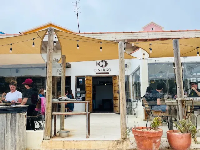 חצר מקורה ביריעות בד ונורות שרשרת, סועדים סביב שולחנות מול כניסה לבנה