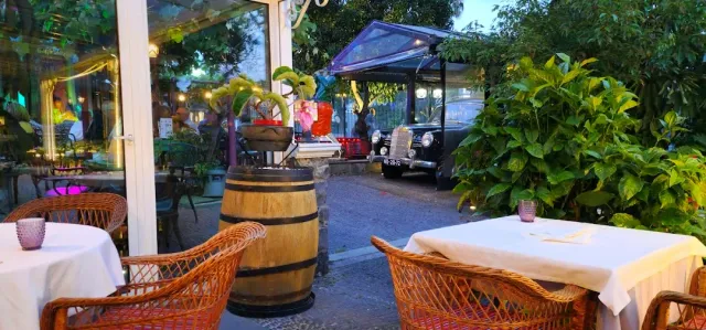 טרסה עם כורסאות נצרים ומפות לבנות סביב חבית עץ בין צמחייה