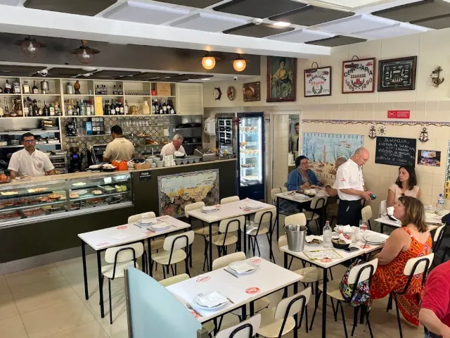 חלל שוקק עם דלפק תצוגה, שולחנות לבנים וסועדים לצד הקיר