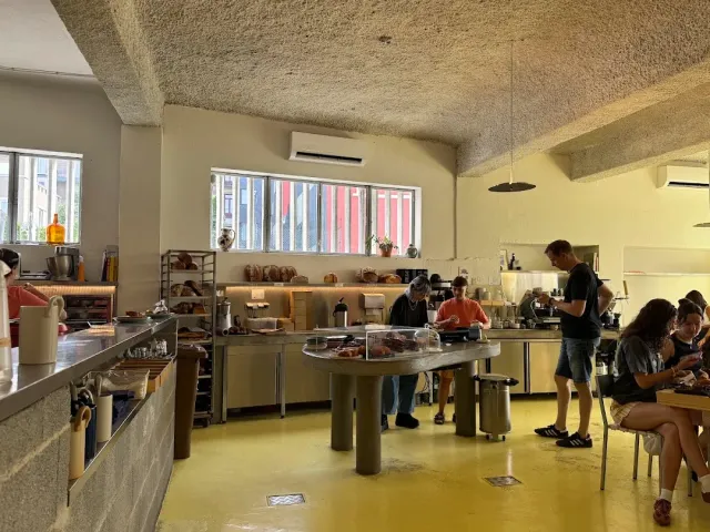 חלל עם רצפה צהובה, תקרת בטון, דלפק מרכזי עם ויטרינה, עובדים ולקוחות