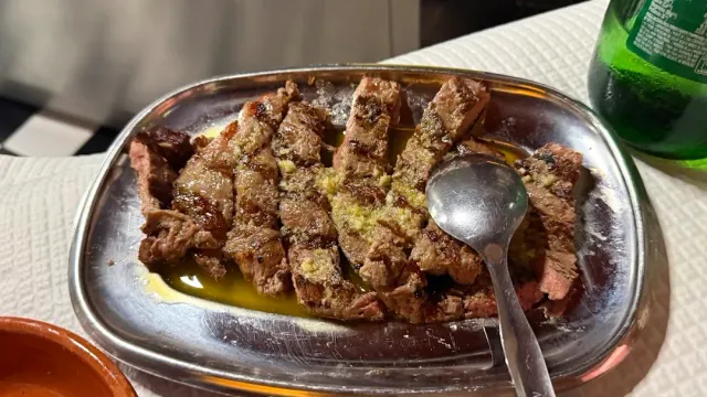מגש מתכת עם רצועות בשר צלוי בשמן וכף מונחת לצידן