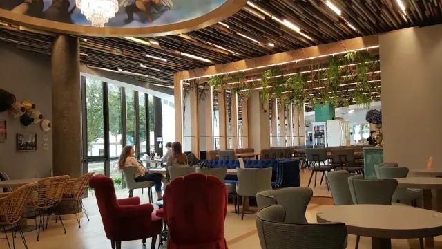 אולם ישיבה מרווח עם צמחים תלויים, כורסאות אדומות ושולחנות עגולים