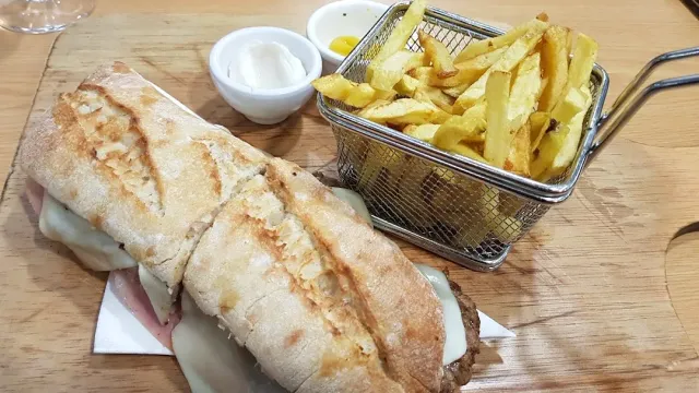 כריך בלחם כפרי חצוי לצד סלסלת צ׳יפס ושתי קעריות רוטב
