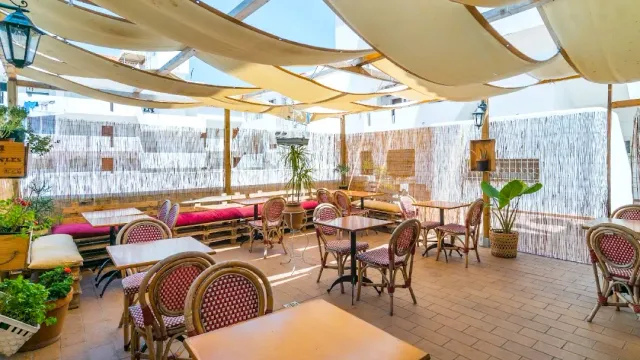 חצר מקורה ביריעות בד עם כיסאות קש, ספסלים אדומים ומחיצות קנים