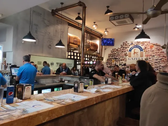 דלפק עץ ארוך עם סועדים, מיכל נחושת וקיר מכוסה תצלומים קטנים