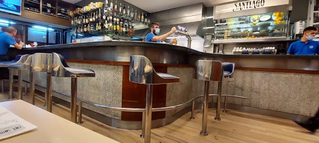 דלפק מעוגל עם שרפרפי מתכת, מדפי בקבוקים ועובדים מאחורי הבר