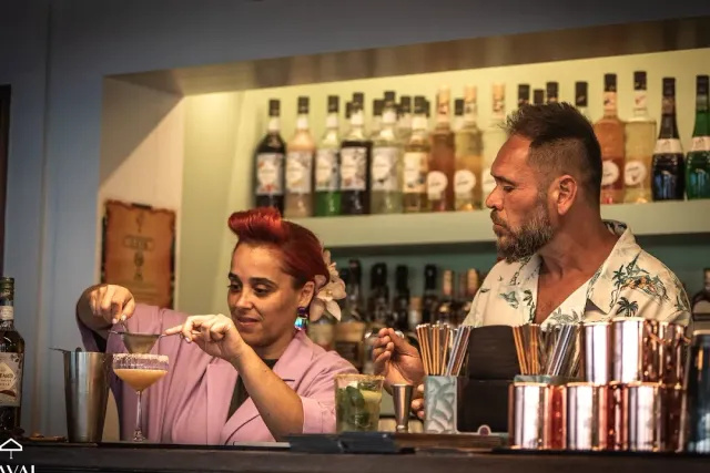 שני ברמנים מכינים משקאות מאחורי הדלפק מול מדף בקבוקים