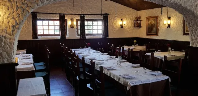 חדר מקומר בקירות אבן עם שולחנות ארוכים במפות לבנות ומנורות קיר