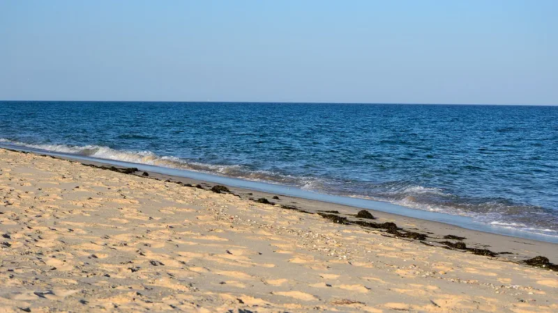 רצועת חול זהוב רחבה וריקה לאורך מים כחולים ורגועים