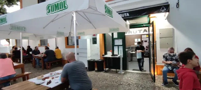 חצר מרוצפת עם שמשיות לבנות, ספסלי עץ וסועדים ליד חלון הגשה