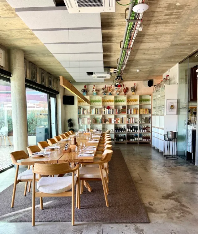 שולחן ערוך ארוך על שטיח, מולו כוננית ספרים, כוסות צבעוניות ובקבוקי יין