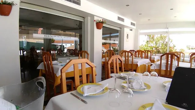 אולם בהיר עם מפות לבנות, מפיות צהובות וכיסאות עץ מול חלונות גדולים