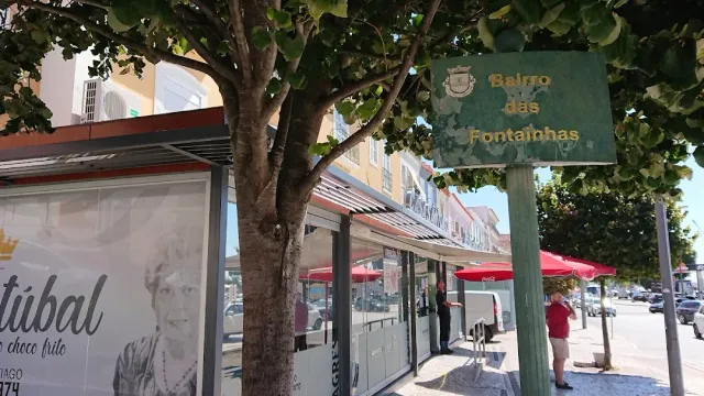 רחוב עם עץ גדול, שלט ירוק ודוכנים מקורים עם שמשיות אדומות