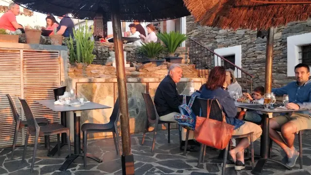 טרסה עם שמשיות קש וקירות אבן, סועדים יושבים באור אחר הצהריים