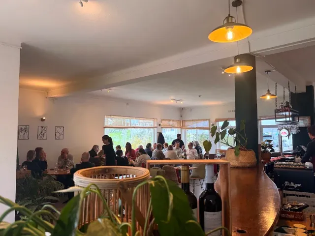חלל מלא סועדים עם מנורות פליז תלויות, דלפק עץ וצמחייה בחזית