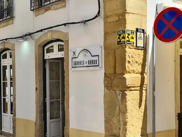 חזית לבנה בסמטה עם דלת קשת צרה, שלט תלוי ופינת אבן מסותתת