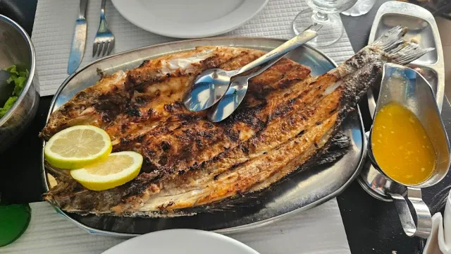 דג שלם צלוי ופתוח על מגש מתכת עם פלחי לימון ורוטב