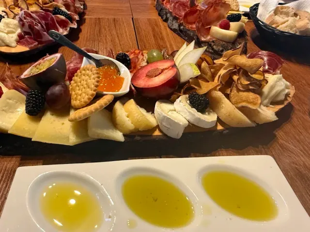 מגש עץ עמוס גבינות, נקניקים, פירות יער ופריכיות לצד שלוש קעריות שמן זית