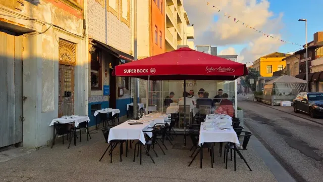 שולחנות רחוב עם מפות לבנות ושמשייה אדומה מול בניין מצופה אריחים באור שקיעה
